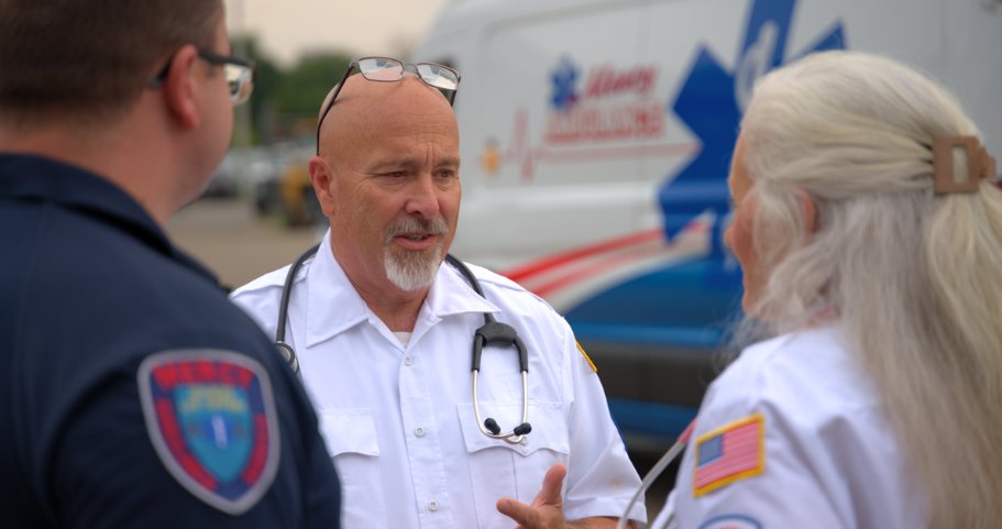 Steve Frisbie in his paramedic uniform talking with two EMS colleagues beside an ambulance